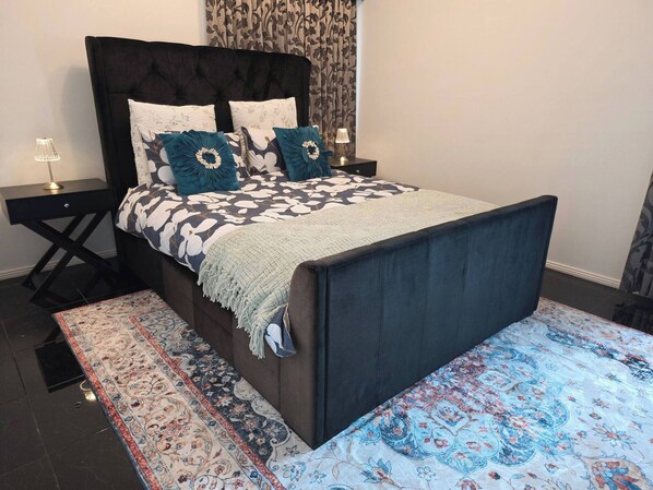 Un lit avec une tête de lit sombre, une couvre-lit à motifs et des coussins décoratifs.