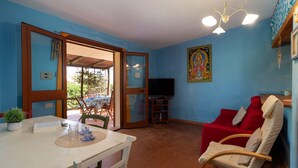 Una stanza con un tavolo da pranzo, un divano rosso, una TV e una ventola a soffitto.