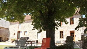 A stone building with a large tree in front, outdoor seating, and a sign indicating a bed and breakfast. - Gîte "La Picolina" near Lac des Fades (Charensat)