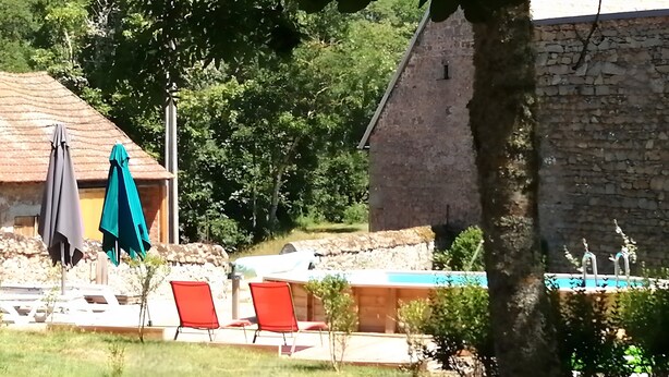 A pool area with lounge chairs, a stone building, and a wooden structure in the background. - Gîte "La Picolina" near Lac des Fades (Charensat)