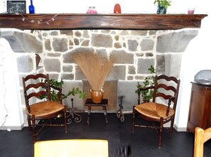 A stone fireplace with two wooden chairs, a vase, and a small table.