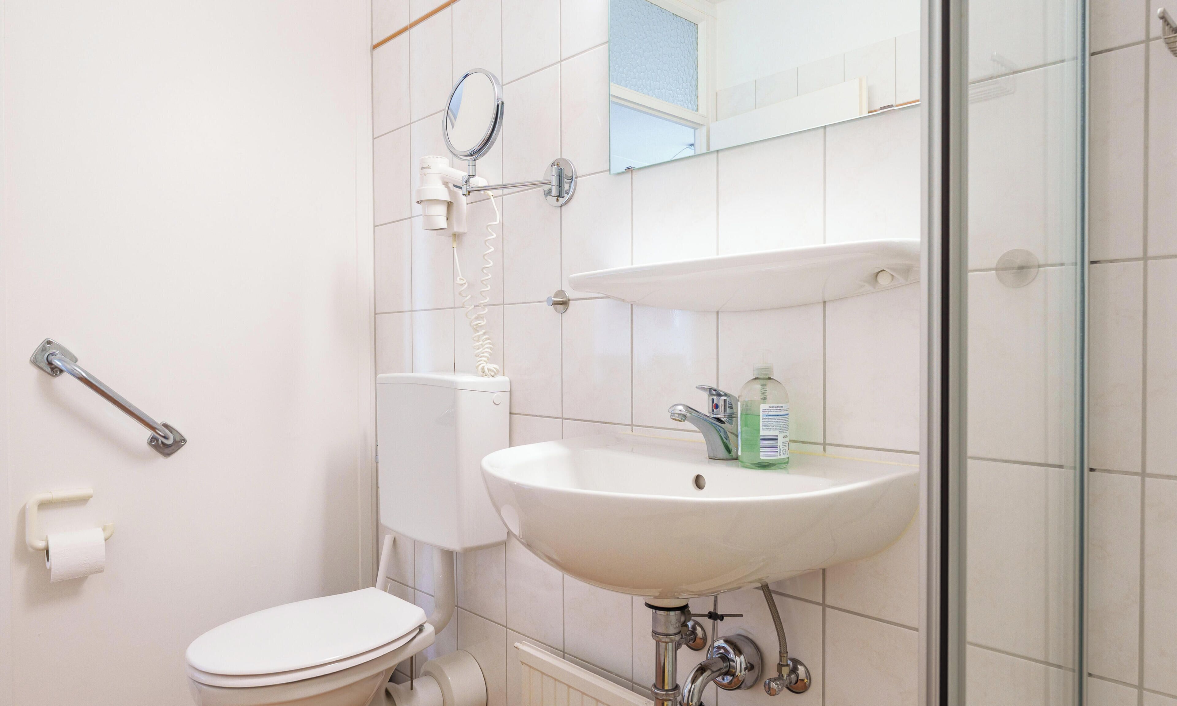 Un baño con inodoro, lavabo, espejo y ducha.