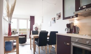 A modern kitchen with a dining area, a coffee machine, and a view of the outdoors. - Deichblick Vacation Rental (Schönberg (Holstein))
