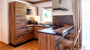 A modern kitchen with wooden cabinetry, a central island, bar stools, and a window providing natural light. - Rauris Penthouse With Fireplace (Rauris)
