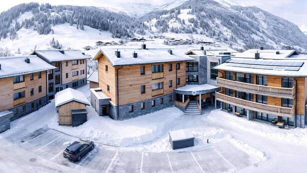 A modern ski resort with multi-story buildings, a parking area, and snow-covered mountains in the background. - Rauris Penthouse With Fireplace (Rauris)