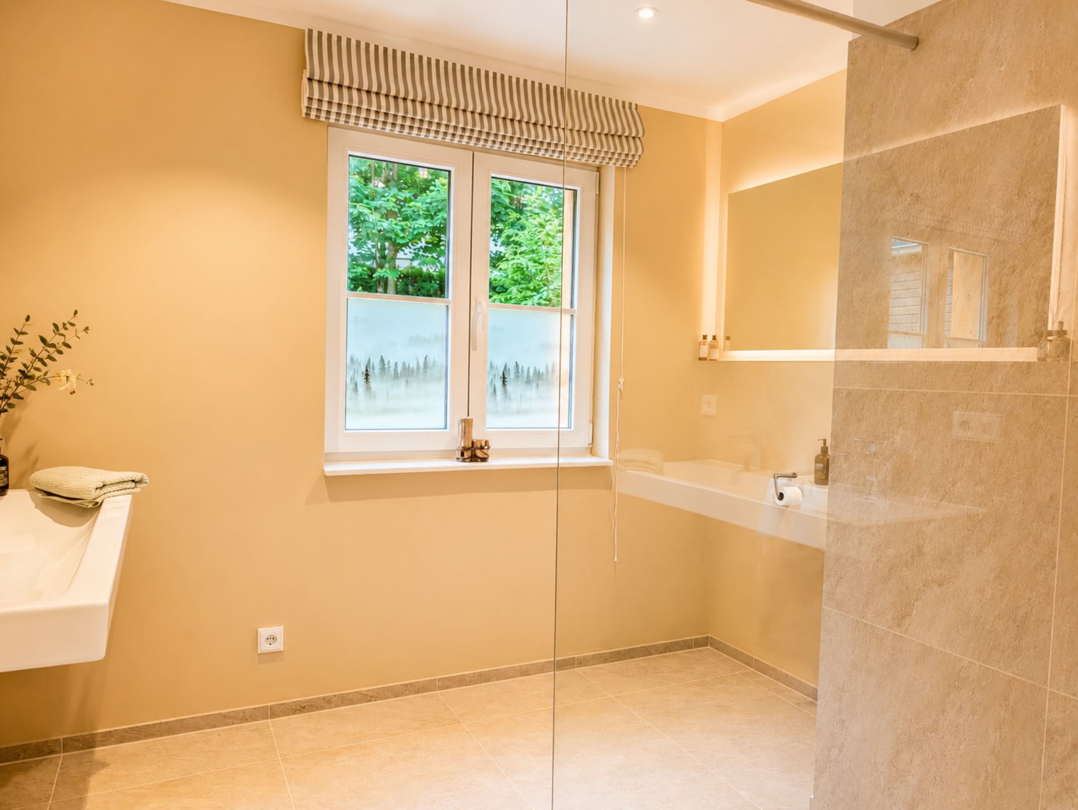 A bathroom with a window, a sink, a mirror, and a shower area.