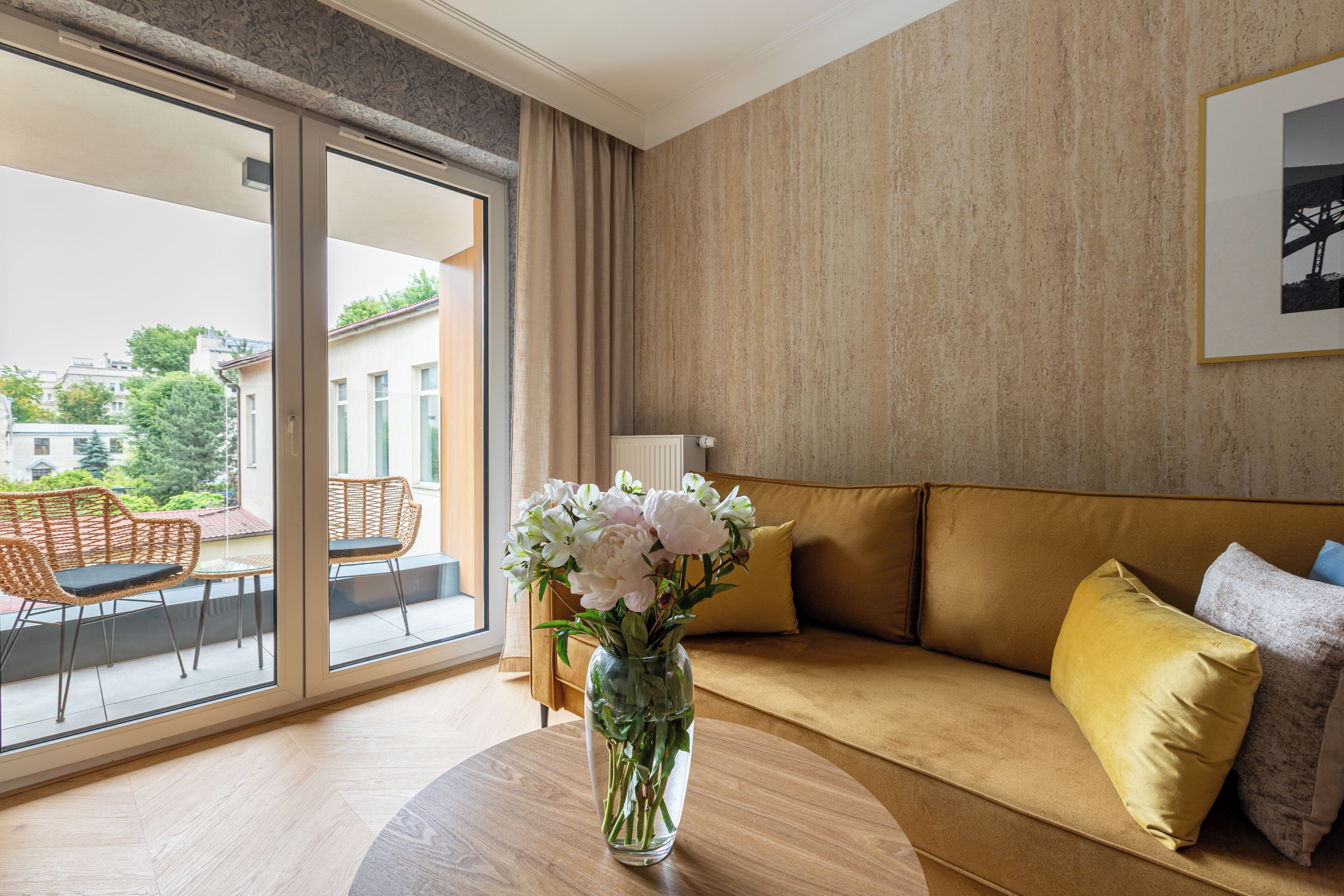 Quarto com sofá, um vaso de flores, uma mesa e vista através de uma porta de vidro.