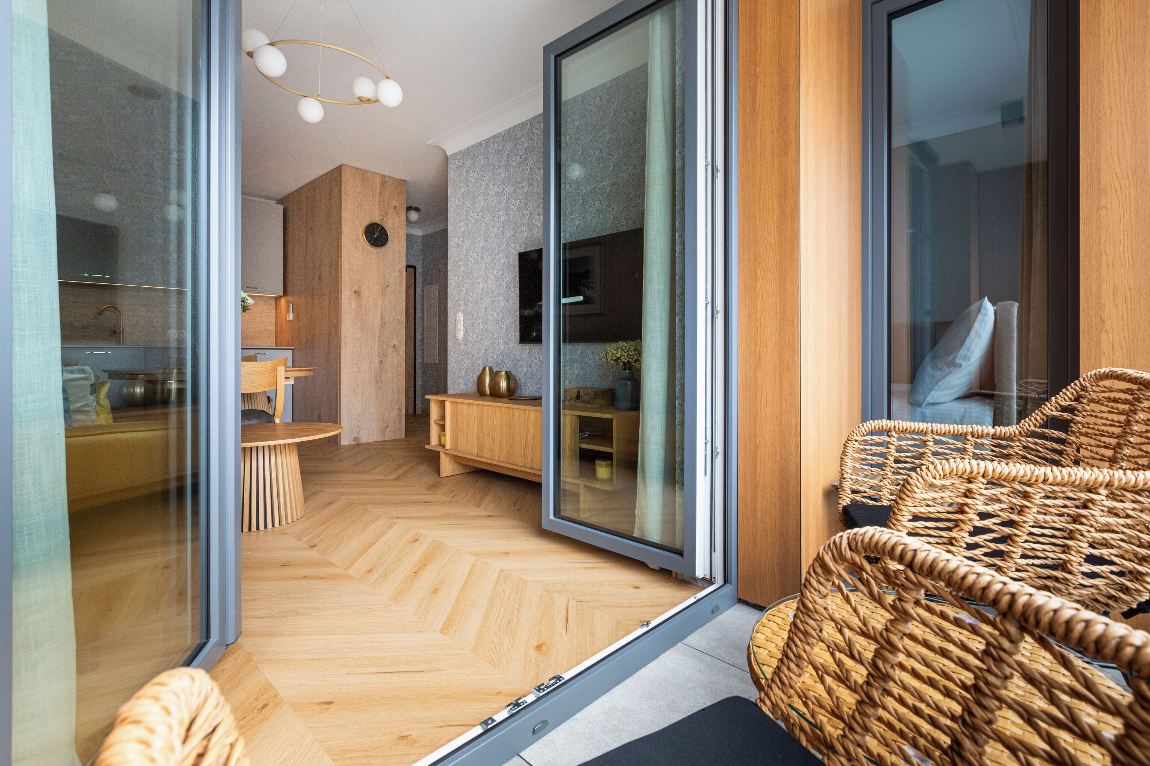 Um interior moderno com piso em padrão herringbone, uma cadeira de vime e uma porta de vidro deslizante que dá para uma cozinha.