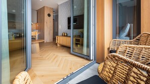 Un intérieur moderne avec un parquet en chevrons, un fauteuil en osier et une porte-fenêtre coulissante donnant sur un espace cuisine.