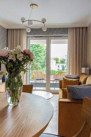 Ein modernes Wohnzimmer mit Esstisch, einer Couch, einer Blumenvase und Blick durch eine Glastür.