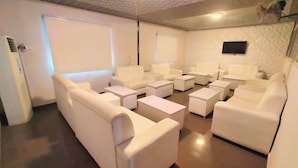 Una habitación con sofás blancos, mesitas pequeñas, un televisor montado en la pared y un techo con diseño.
