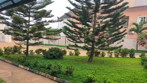 Un jardín ajardinado con diversas especies de árboles y arbustos, un sendero pavimentado y un edificio con tejado de tejas al fondo.