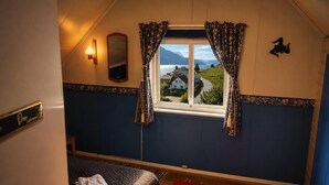 A room with a bed, a window with curtains, a wall-mounted lamp, and a view of houses and mountains. - Room-casa Hauge B&B Sunrise Room (Gloppen)