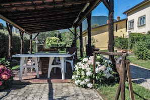 An outdoor patio with a table and chairs, surrounded by greenery and a building in the background. - Case a Stratola (Montella)