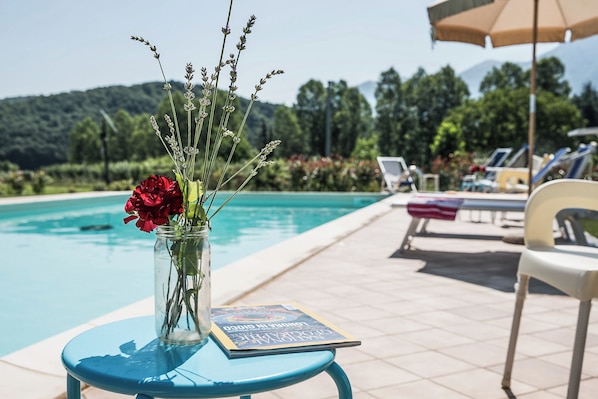 A poolside table with a vase of flowers and a magazine, surrounded by lounge chairs and a pool. - Case a Stratola (Montella)