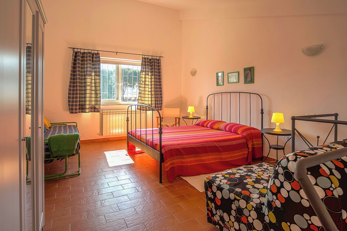 A bedroom with a bed, a chair, a table, and a window with curtains.