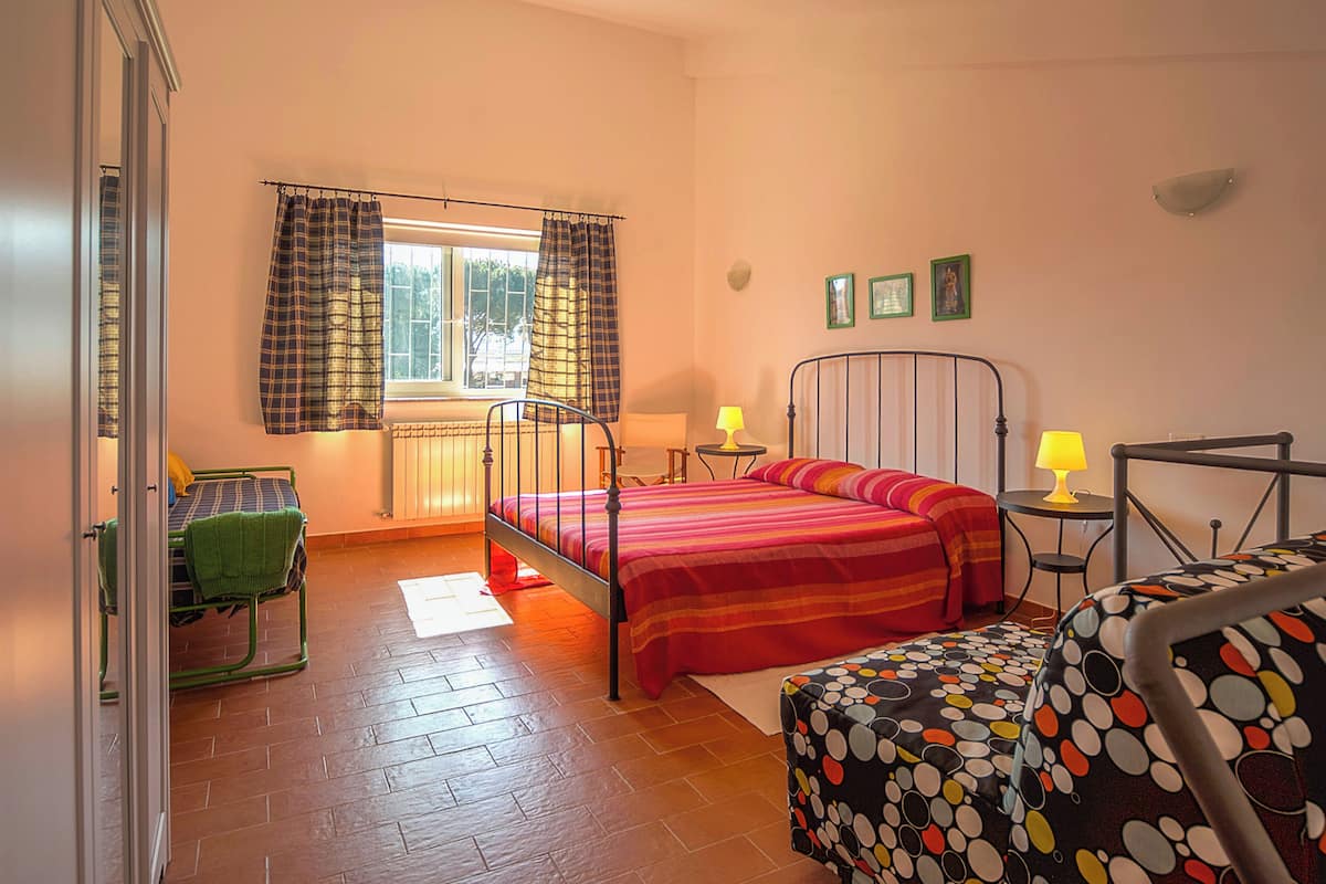 A bedroom with a bed, a chair, a table, and a window with curtains.