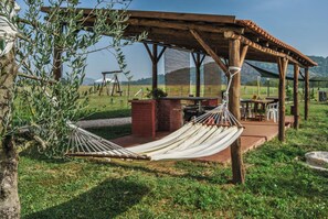 A hammock under a wooden pergola, a brick fireplace, and a table with chairs in a grassy outdoor setting. - Case a Stratola (Montella)