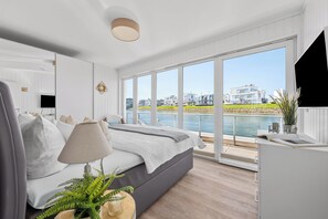Ein modernes Schlafzimmer mit Bett, Nachttischlampe und Blick auf ein Gewässer.