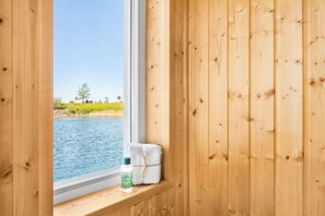 A wooden cabin with a window overlooking a body of water, a towel, and a bottle. - On Board 2 in the Baltic Sea resort of Olpenitz: Houseboat with a rooftop terrace and a view of the Schleif River (Olpenitz)