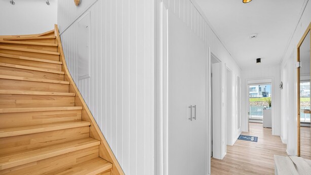 Een modern interieur met een houten trap, witte muren en uitzicht naar buiten.