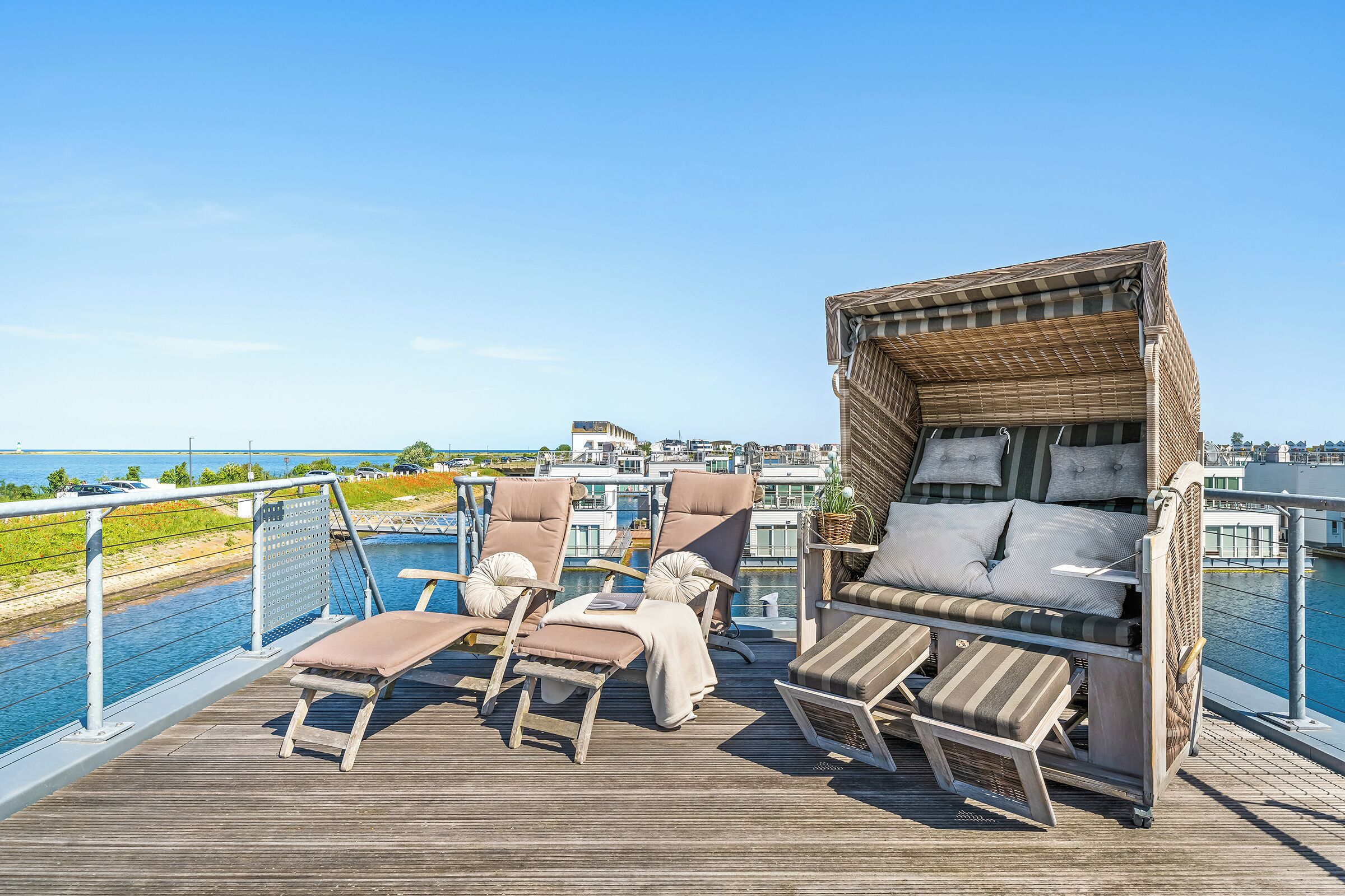 A deck with lounge chairs and a wicker sofa overlooking a marina.