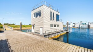 Ein Gebäude am Wasserufer mit einer Holzterrasse, einem kleinen Steg und blauem Himmel.