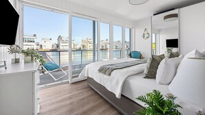 Ein modernes Schlafzimmer mit großem Fenster, einem Bett, einem Schreibtisch und Blick auf ein Gewässer.