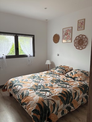 A bedroom with a bed, a window with curtains, a wall-mounted lamp, and decorative wall art.