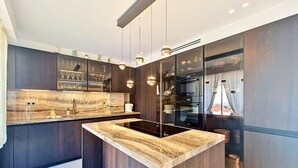 Une cuisine moderne dotée d’un îlot central, de meubles de rangement aux couleurs sombres et d’un éclairage suspendu.