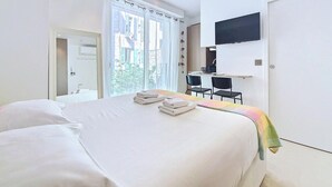 Une chambre d’hôtel avec un lit, un bureau, une chaise, une télévision et une fenêtre avec des rideaux.