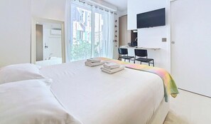 Ein Hotelzimmer mit Bett, Schreibtisch, Stuhl, Fernseher und einem Fenster mit Vorhängen.