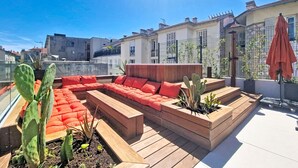 Une terrasse sur le toit avec une plateforme en bois, des sièges rembourrés de couleur rouge et des cactus.