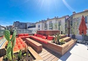 Eine Dachterrasse mit Holzboden, rotem Sitzmöbel mit Kissen und Kakteen.