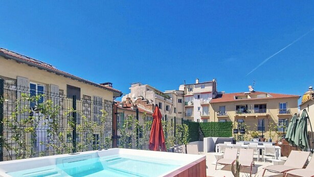 Un espace piscine aménagé sur le toit, avec des chaises longues et des parasols, entouré d’immeubles dotés de balcons.