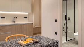 Casa de banho moderna com chuveiro envidraçado, pia branca e cadeira de madeira com um livro.