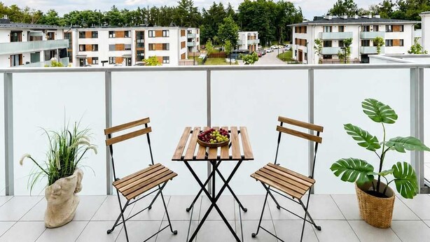 A balcony with a table and chairs, a potted plant, and a view of apartment buildings.