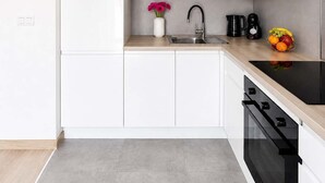 A modern kitchen with white cabinets, a stainless steel sink, a black faucet, a coffee maker, and a fruit bowl.