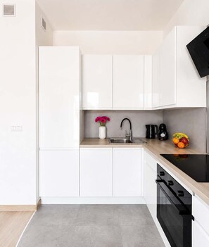 A modern kitchen with white cabinets, a stainless steel sink, a black faucet, a coffee maker, and a fruit bowl. - Lumina Apart near ZOO in Lodz with Parking (Łódź)