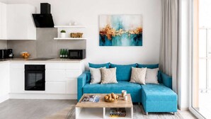 A modern living room with a blue sofa, a coffee table, and a kitchen area with white cabinets and a black range hood.