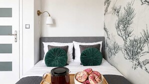 Ein Schlafzimmer mit einem Bett, einem Tablett mit Tasse und Donuts, einer Wandlampe und einer Tür mit Lichtschalter.