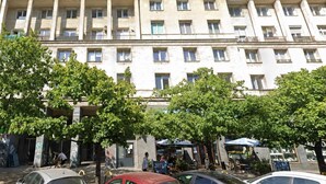 Ein mehrstöckiges Gebäude mit Balkonen, einem Café im Erdgeschoss und abgestellten Autos.