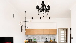 Ein modernes Wohnzimmer mit Flachbildfernseher, einem runden Couchtisch, einer Couch mit Kissen, einem Essbereich mit Stühlen und einer Küche inklusive Mikrowelle und Backofen.