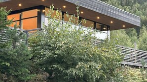 A modern building with a sloped roof, large windows, and a view of a forested hillside. - Architect drawn home with amazing view over Nisser (Treungen)