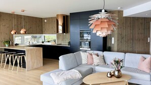A modern living space with a kitchen, a grey sectional sofa, a coffee table, and a pendant light. - Architect drawn home with amazing view over Nisser (Treungen)