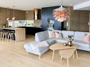 A modern living space with a kitchen, a grey sectional sofa, a coffee table, and a pendant light. - Architect drawn home with amazing view over Nisser (Treungen)