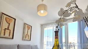 Ein modernes Wohnzimmer mit einer Couch, einem Tisch mit einer Flasche und einem Weinglas, sowie zwei abstrakten Bildern an der Wand.