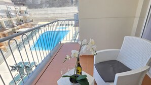 Ein Balkon mit Blick auf einen Swimmingpool, einer Topforchidee und Korbmöbeln.