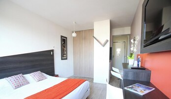 A modern hotel room with a bed, a desk, a television, and a mirror.
