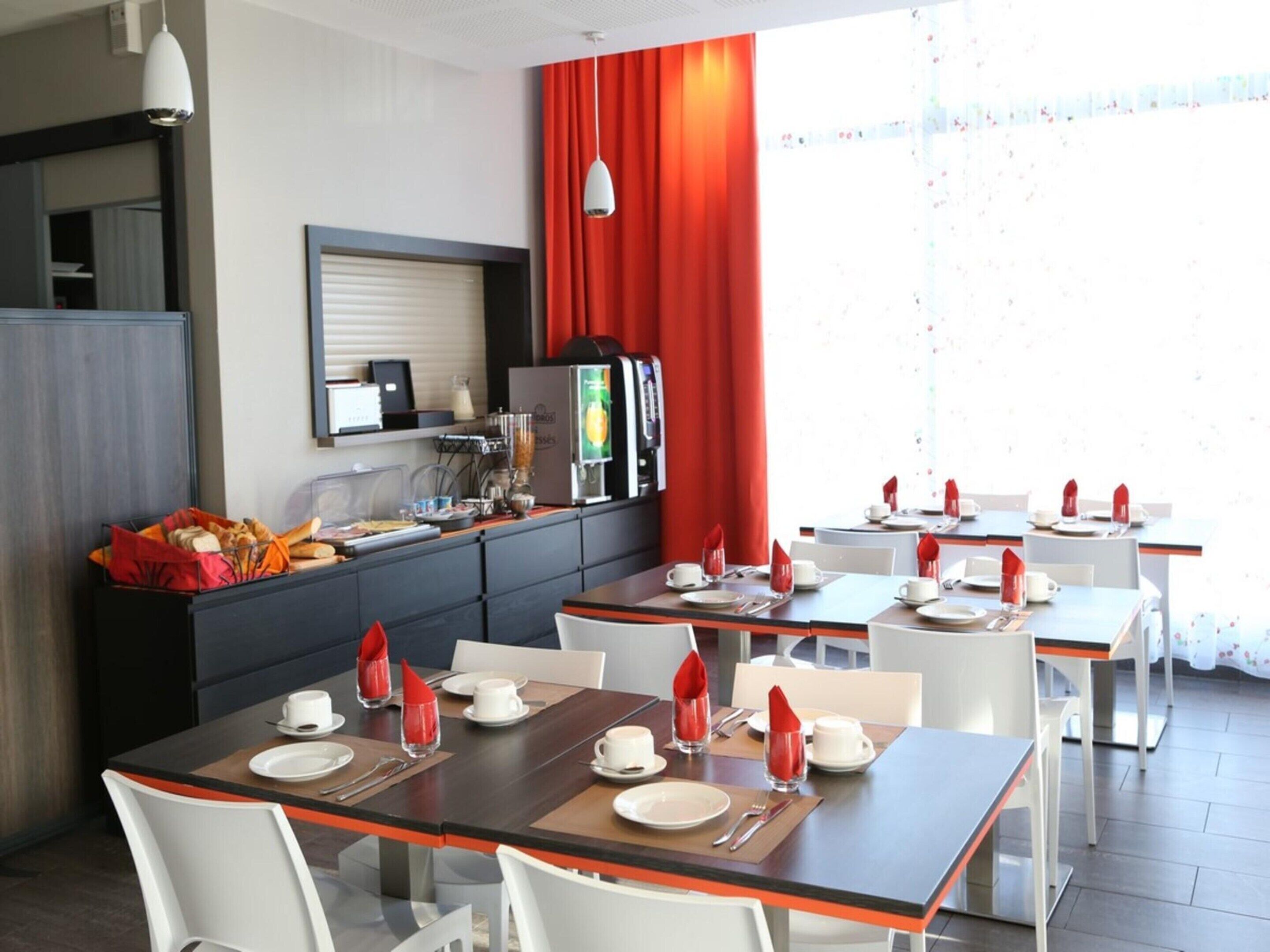 Un comedor de hotel con mesas dispuestas para el desayuno, una máquina de café y un refrigerador.